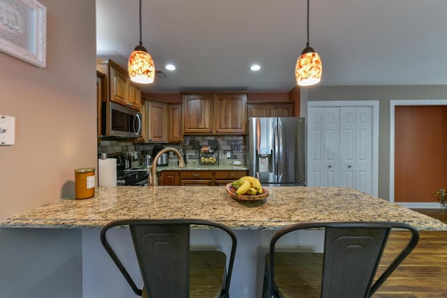 kitchen with light stone counters, backsplash, stainless steel appliances, a peninsula, and a breakfast bar area