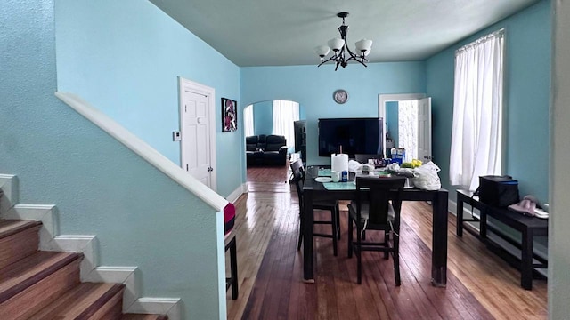 dining space with hardwood / wood-style flooring, stairway, a notable chandelier, and arched walkways