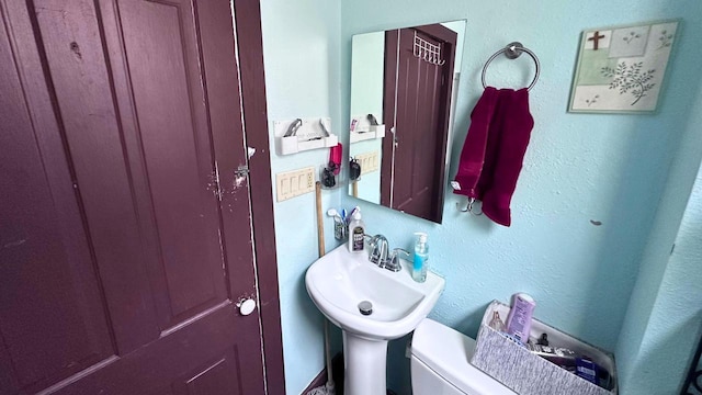 half bathroom with a sink, toilet, and a textured wall