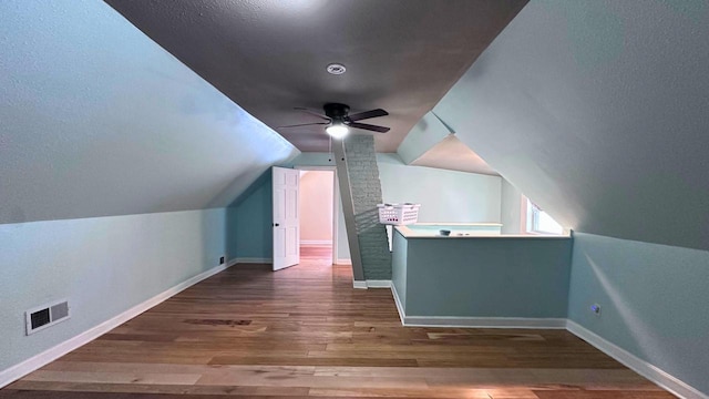 additional living space featuring a ceiling fan, wood finished floors, visible vents, baseboards, and lofted ceiling