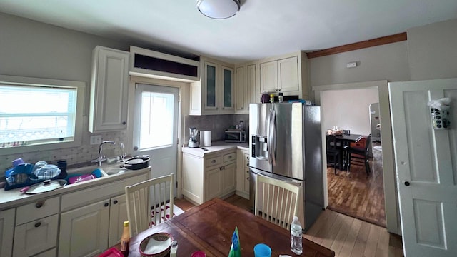 kitchen with light wood-style flooring, light countertops, glass insert cabinets, stainless steel refrigerator with ice dispenser, and backsplash