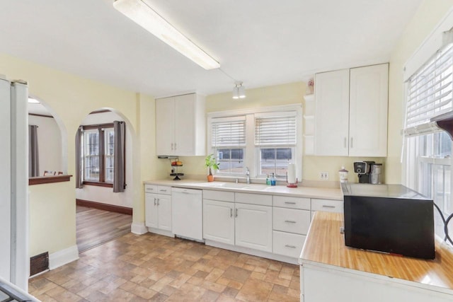 kitchen featuring a sink, white appliances, arched walkways, white cabinets, and baseboards