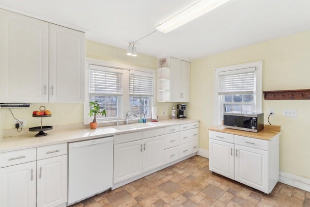 kitchen with stainless steel microwave, stone finish flooring, dishwasher, white cabinets, and a sink