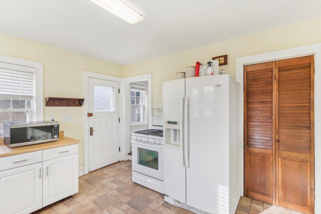 kitchen featuring white appliances, white cabinetry, light countertops, and stone finish floor