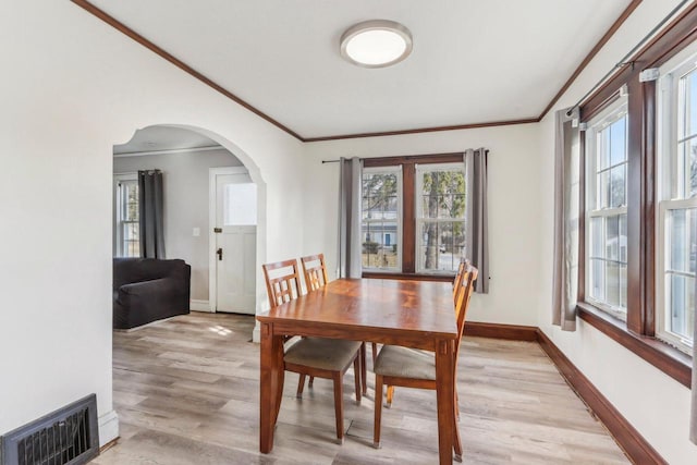 dining space with visible vents, baseboards, ornamental molding, light wood-style floors, and arched walkways