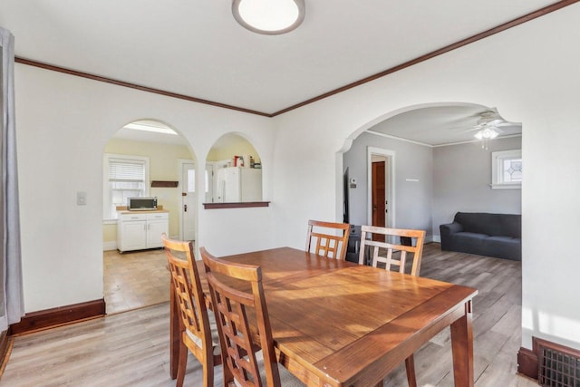 dining room with visible vents, a ceiling fan, arched walkways, light wood finished floors, and baseboards