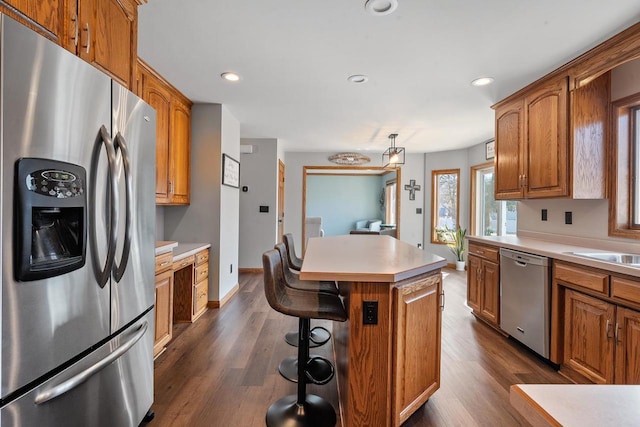 kitchen with a kitchen island, light countertops, dark wood-style floors, brown cabinetry, and stainless steel appliances