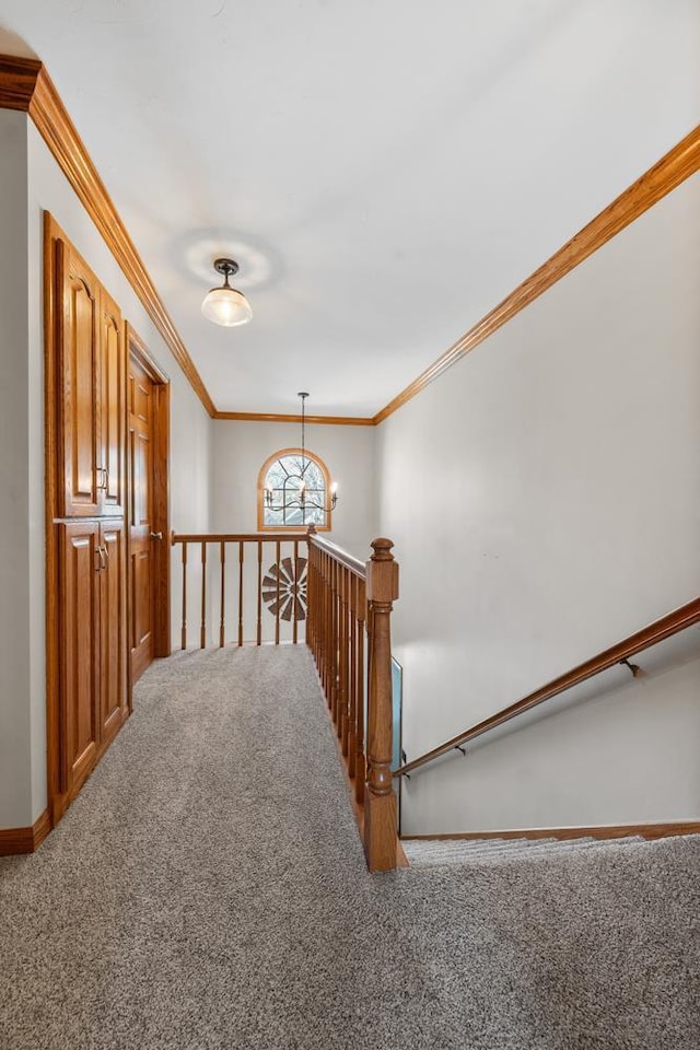 corridor with baseboards, ornamental molding, an upstairs landing, carpet floors, and a notable chandelier