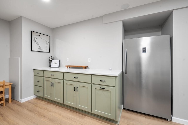 kitchen with light wood-type flooring, freestanding refrigerator, light countertops, green cabinetry, and baseboards