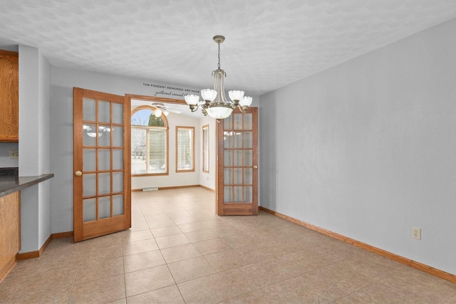 unfurnished dining area featuring a notable chandelier, french doors, and baseboards