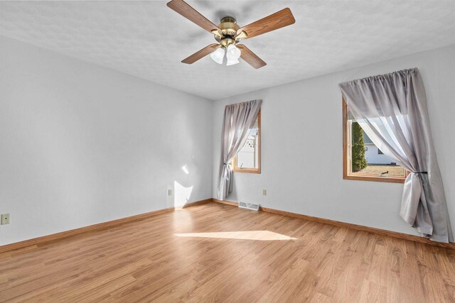 spare room with light wood-type flooring, visible vents, baseboards, and a ceiling fan