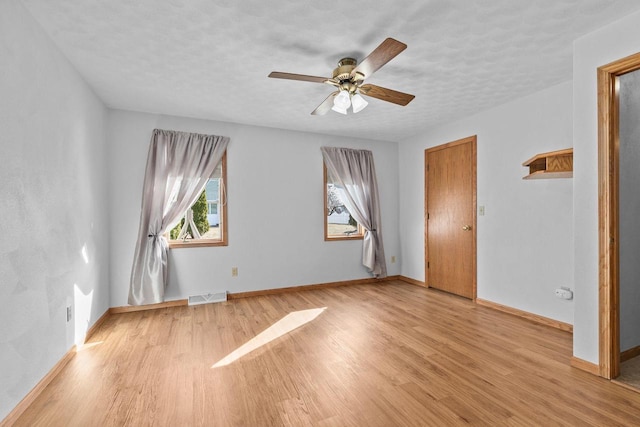 empty room featuring light wood finished floors, visible vents, ceiling fan, and baseboards