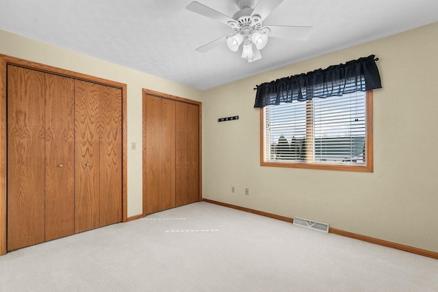 unfurnished bedroom featuring visible vents, two closets, carpet, baseboards, and a ceiling fan