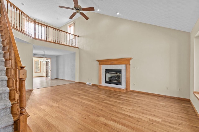 unfurnished living room with baseboards, ceiling fan with notable chandelier, light wood-type flooring, and a tile fireplace