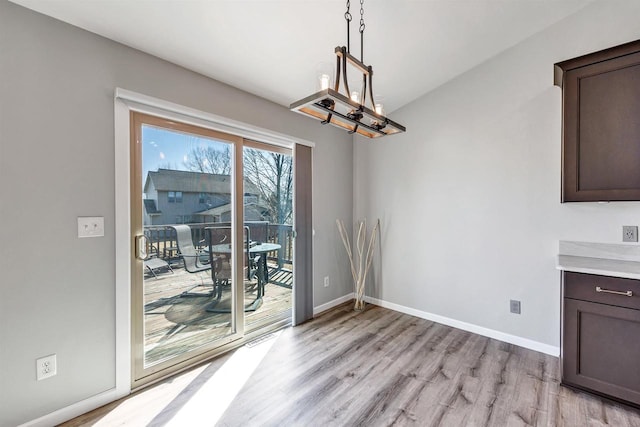 unfurnished dining area with light wood-type flooring, baseboards, and a notable chandelier