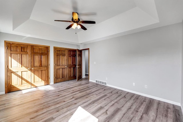 unfurnished bedroom featuring light wood-type flooring, visible vents, two closets, a tray ceiling, and baseboards