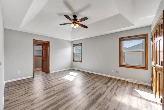 unfurnished bedroom featuring a tray ceiling, multiple windows, and wood finished floors