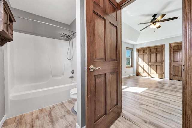 bathroom featuring toilet, shower / bathtub combination, baseboards, and wood finished floors