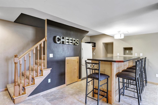 kitchen featuring dark countertops, a breakfast bar area, freestanding refrigerator, and baseboards