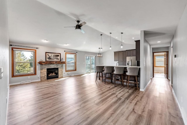 living room featuring a ceiling fan, visible vents, light wood-style flooring, a fireplace, and vaulted ceiling