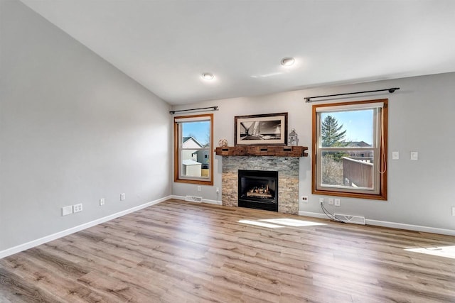 unfurnished living room featuring visible vents, baseboards, vaulted ceiling, a stone fireplace, and wood finished floors