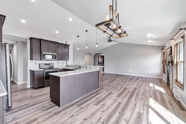 kitchen with arched walkways, appliances with stainless steel finishes, light wood-style floors, and vaulted ceiling