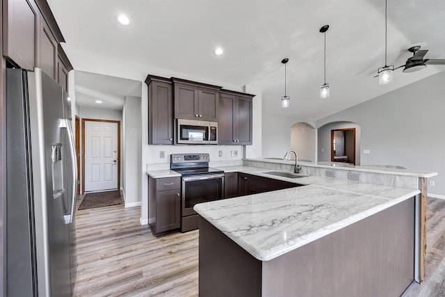 kitchen with a sink, stainless steel appliances, arched walkways, a peninsula, and dark brown cabinets