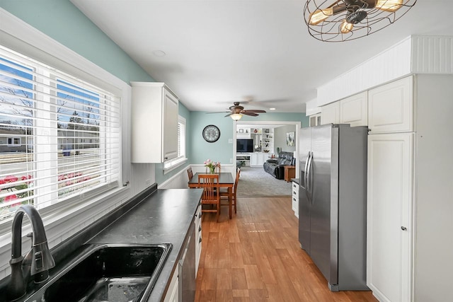 kitchen with dark countertops, stainless steel fridge with ice dispenser, light wood-style flooring, white cabinets, and a sink