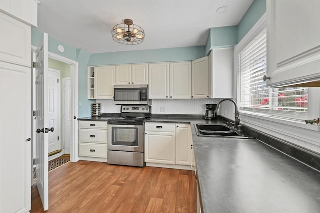 kitchen with a sink, light wood-style floors, appliances with stainless steel finishes, and white cabinetry