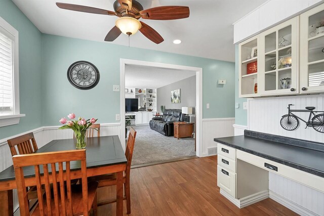 dining room with built in features, a ceiling fan, dark wood-style floors, and wainscoting