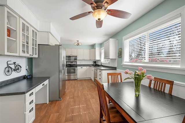 kitchen featuring light wood finished floors, a sink, glass insert cabinets, appliances with stainless steel finishes, and dark countertops