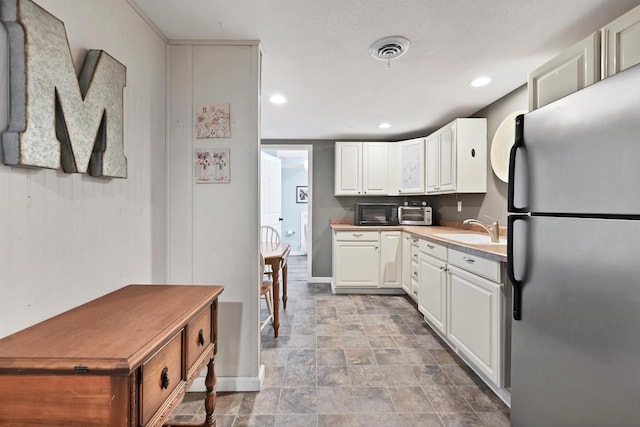 kitchen featuring visible vents, light countertops, freestanding refrigerator, white cabinets, and a sink