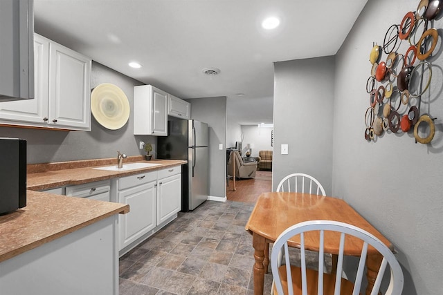 kitchen featuring white cabinetry, visible vents, freestanding refrigerator, and a sink