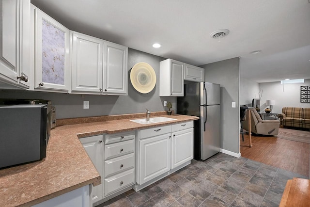 kitchen with white cabinets, freestanding refrigerator, and a sink