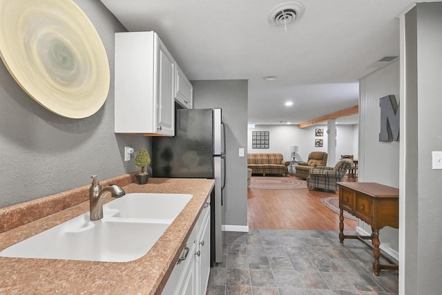 kitchen with baseboards, visible vents, a sink, white cabinets, and open floor plan