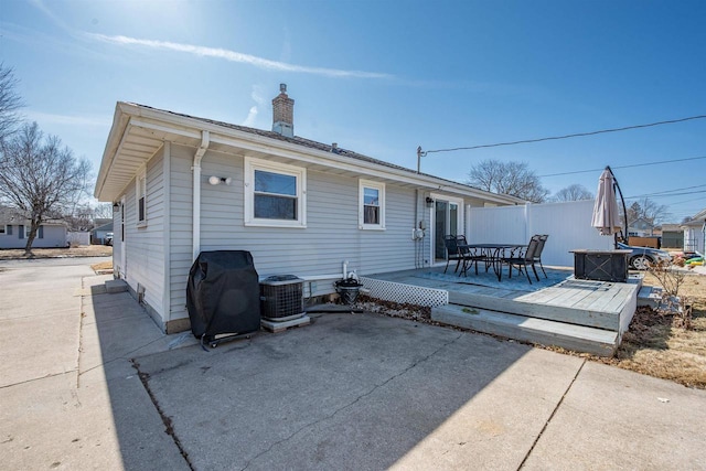 back of property with central air condition unit, fence, a wooden deck, a chimney, and a patio area