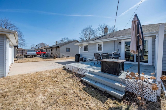 back of house featuring an outdoor fire pit, a chimney, a deck, and roof with shingles