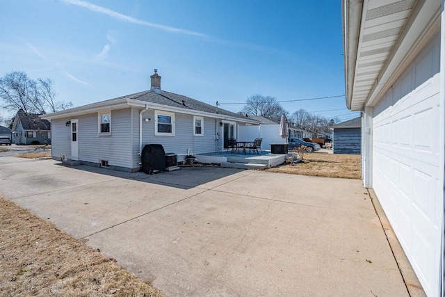 view of side of property featuring a garage, a chimney, a patio, and roof with shingles