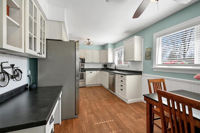 kitchen featuring a sink, stainless steel appliances, dark countertops, and a wainscoted wall