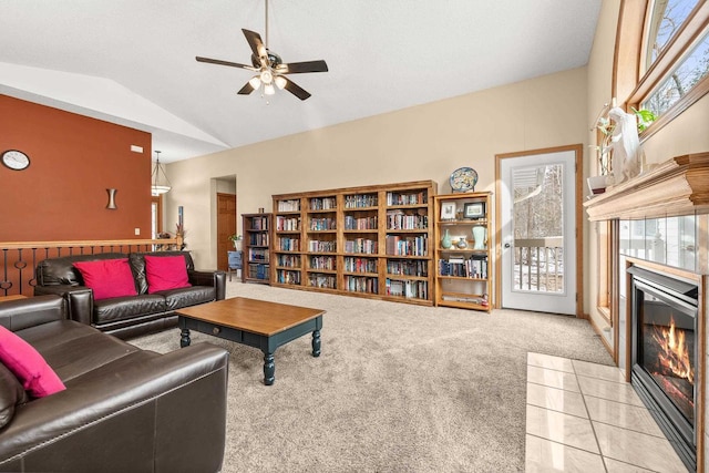 carpeted living room featuring a tiled fireplace, vaulted ceiling, a healthy amount of sunlight, and a ceiling fan