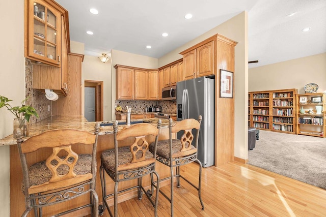 kitchen with a breakfast bar, tasteful backsplash, stainless steel appliances, a peninsula, and glass insert cabinets