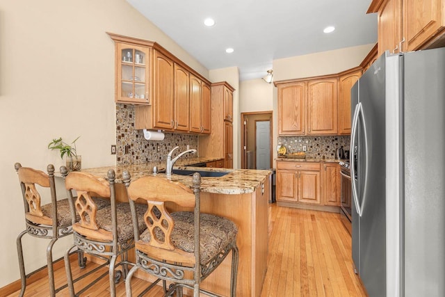 kitchen featuring glass insert cabinets, light wood-type flooring, a peninsula, freestanding refrigerator, and a sink