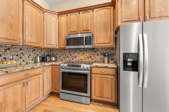 kitchen featuring light stone counters, light wood-style flooring, appliances with stainless steel finishes, and tasteful backsplash