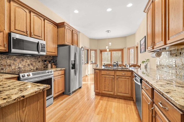 kitchen featuring light wood-type flooring, stainless steel appliances, a peninsula, brown cabinetry, and light stone countertops