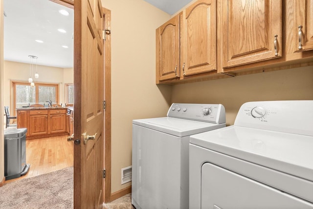 washroom featuring visible vents, light wood-style flooring, washer and clothes dryer, cabinet space, and baseboards