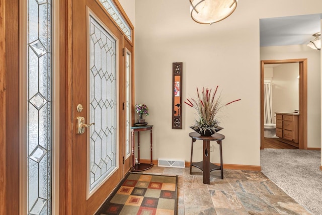 foyer featuring visible vents, baseboards, carpet, and stone finish flooring