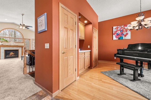 hall featuring a textured ceiling, light wood-type flooring, baseboards, and vaulted ceiling