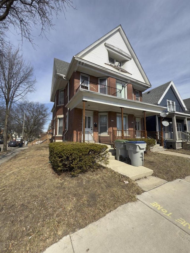 view of front of home featuring brick siding, a porch, and a balcony