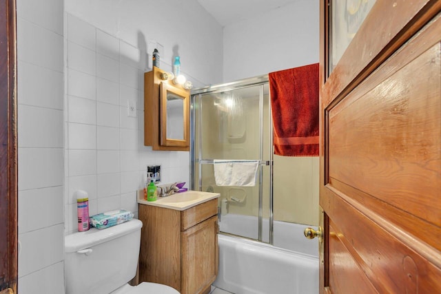 bathroom with shower / bath combination with glass door, tile walls, vanity, and toilet