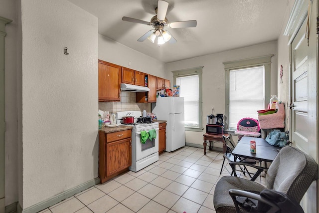 kitchen with under cabinet range hood, tasteful backsplash, white appliances, brown cabinetry, and ceiling fan